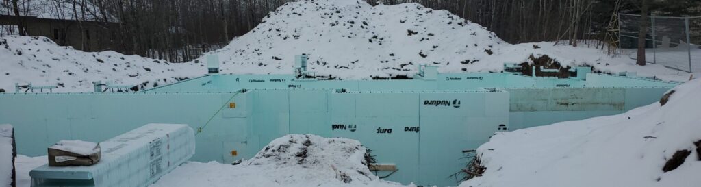 In-progress Nudura ICF foundation construction, set against a snowy landscape. The interlocking Insulated Concrete Forms (ICF) showcase the commitment to energy-efficient building in challenging weather conditions.
