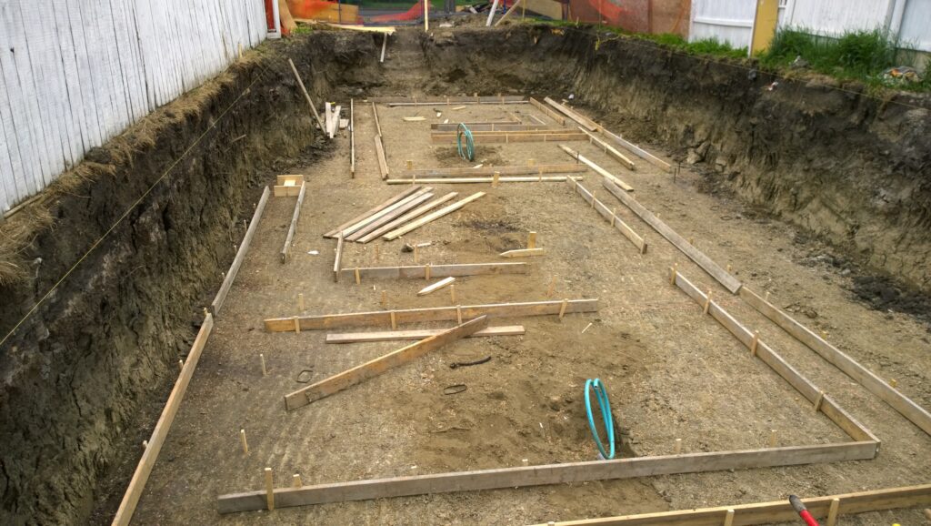 Excavated site with wooden forms being set up for the footings of an ICF foundation, showcasing the meticulous craftsmanship in preparation for a robust and energy-efficient home.