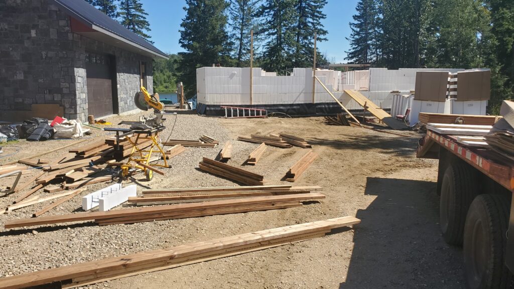 Stacks of pressure-treated lumber for various window sizes on an Advantage ICF cabin construction site, with a visible miter saw, showcasing the meticulous preparation for embedded wood bucks.