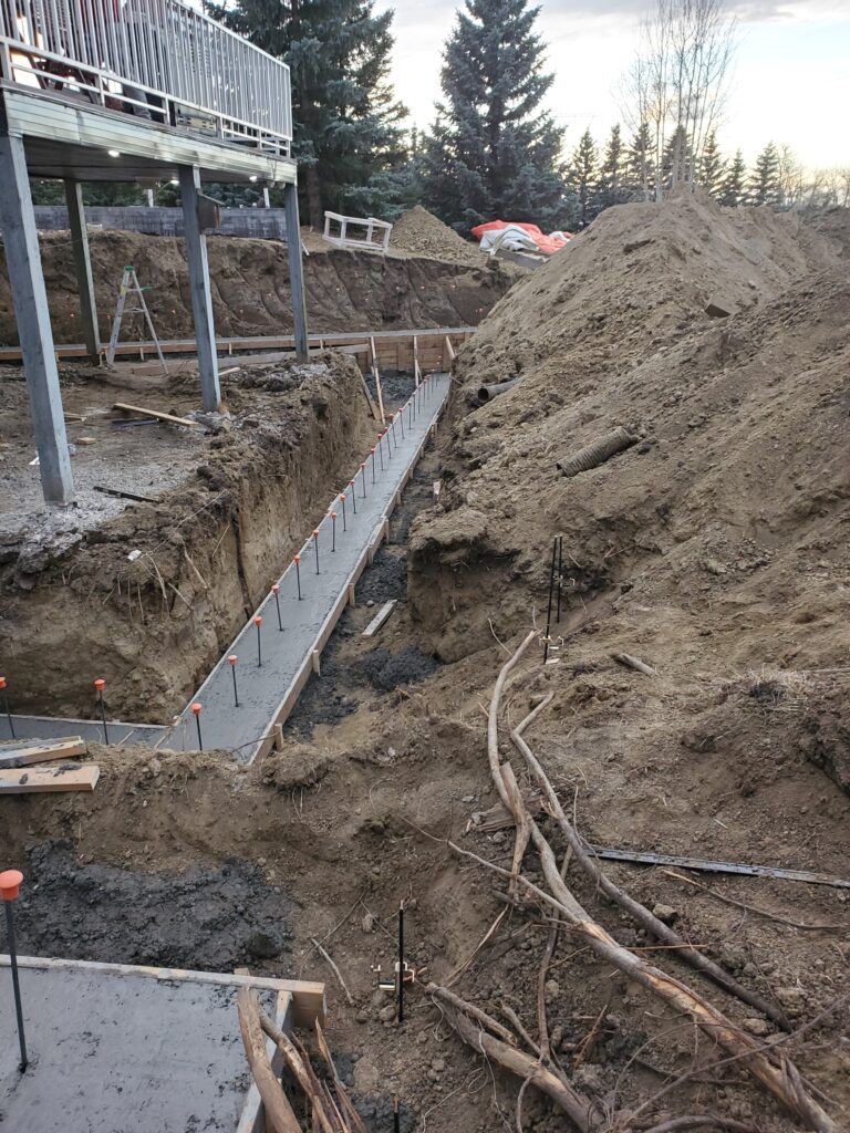 Concrete footing with a protruding rebar dowel at the top center, ready to anchor the upcoming installation of an Insulated Concrete Form (ICF) wall.