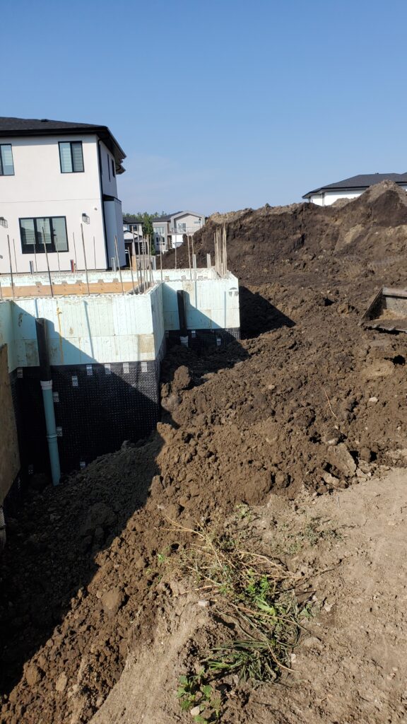 A Nudura ICF basement with visible rainwater leads connected to the storm drain, surrounded by excavated soil.