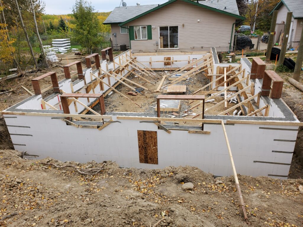 A construction site with the foundation of a building made from Insulated Concrete Forms (ICF), surrounded by wooden supports
